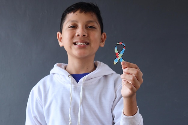 Smiling young boy holding colorful autism awareness ribbon. World Autism Awareness Day.