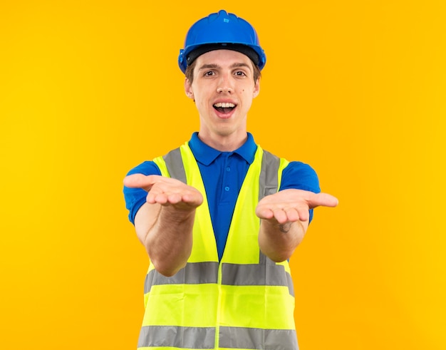 Smiling young builder man in uniform holding out hands at camera 