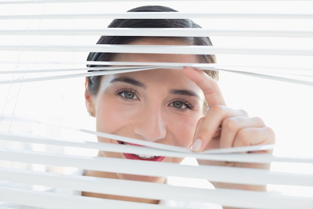 Photo smiling young business woman peeking through blinds