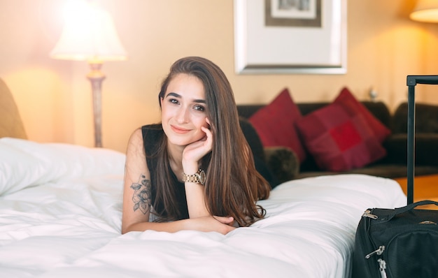 Smiling young businesswoman in bed, girl licks on the bed near the suitcase.