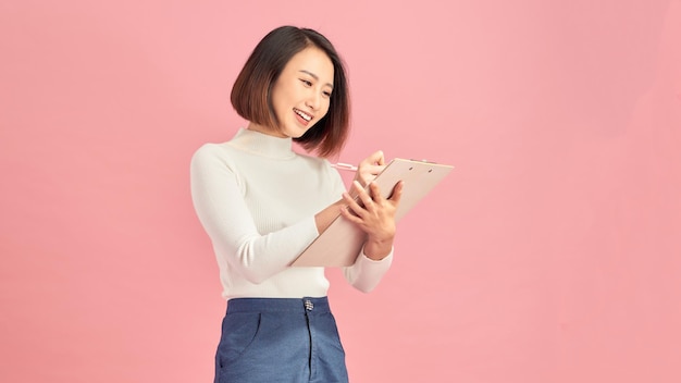 Smiling young businesswoman holding clipboard on pink background