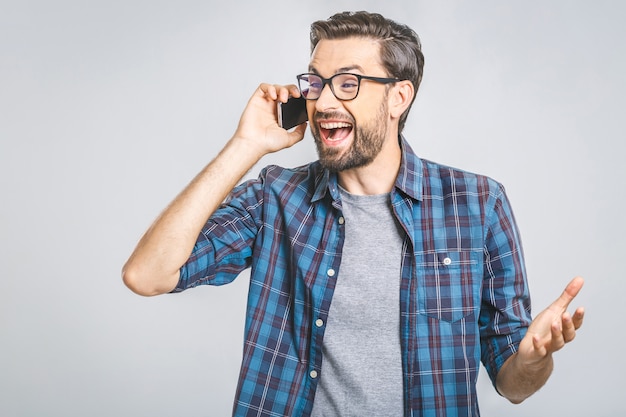 Smiling young casual man talking on the phone on the grey wall. Isolated.