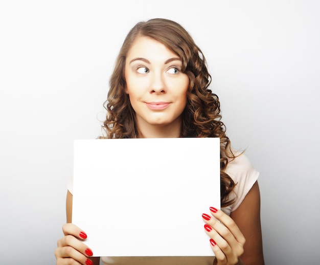 Smiling young casual style woman showing blank signboard over grey background isolated