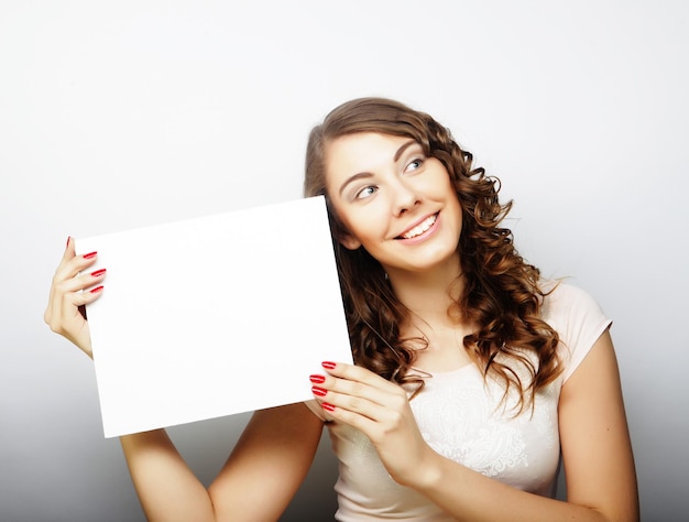 Smiling young casual style woman showing blank signboard over grey background isolated