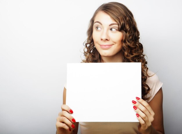 Smiling young casual style woman showing blank signboard over grey background isolated