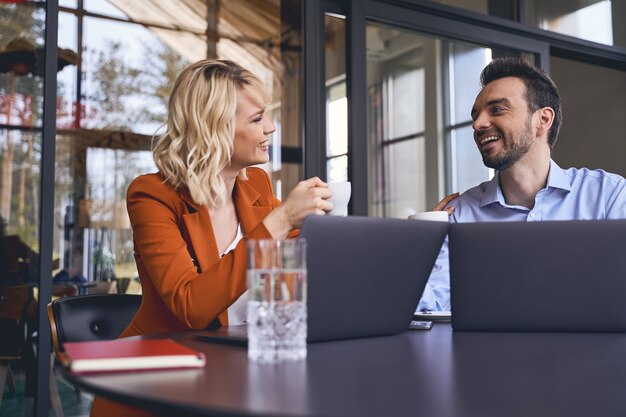 Smiling young Caucasian business lady tapping her handsome cheerful dark-haired male colleague on the shoulder