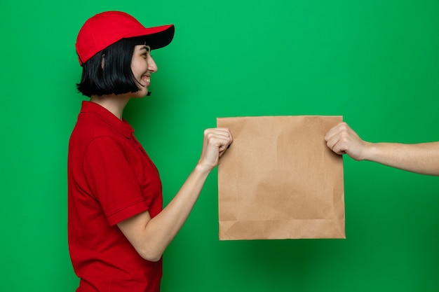 Smiling young caucasian delivery girl giving paper food packaging to someone 