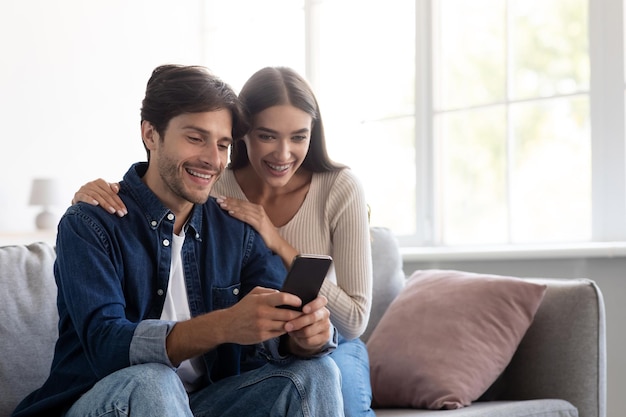 Smiling young caucasian man and woman looking at smartphone together have video call