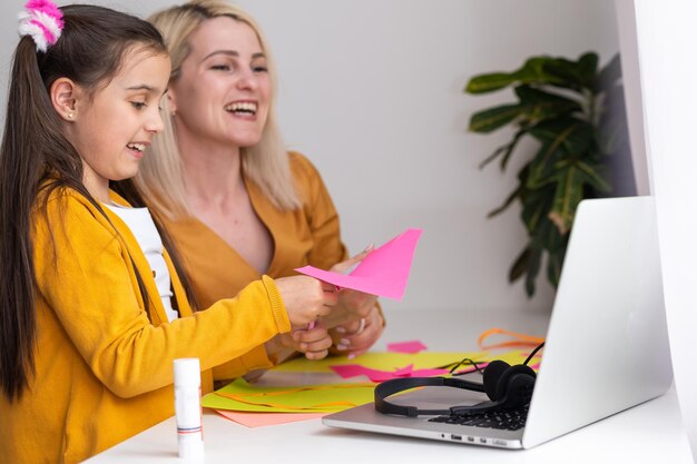 Smiling young Caucasian mom and small daughter sit at home use modern laptop together. Happy mother and little girl child study online talk on video call on computer.