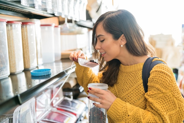 Smiling young Caucasian woman smelling food in scoop at supermarket