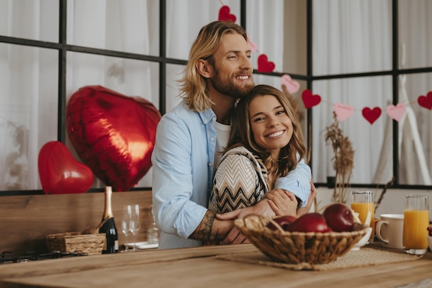 Smiling young couple embracing while celebrating valentines day with red balloons on background