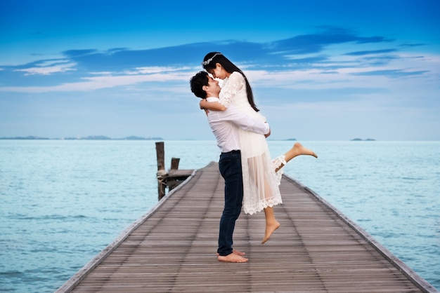 Smiling young couple hug while standing on wooden bridge; wood