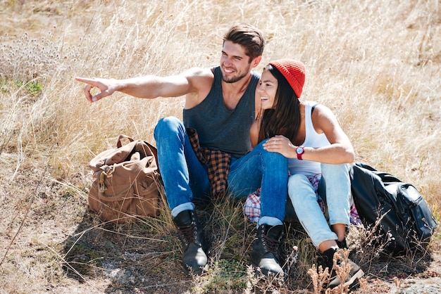 Smiling young couple resting together oudoors and pointing finger