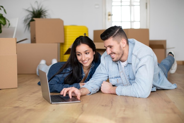 Smiling Young Couple Using Laptop After Moving To Their New Home