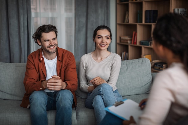 Smiling young european couple on consultation with female doctor psychologist in clinic interior