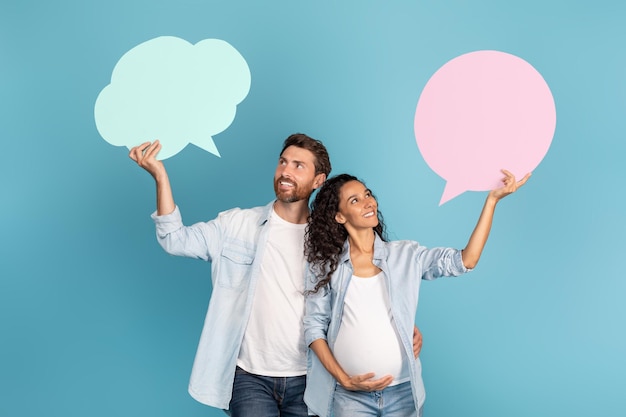 Smiling young european guy and arab pregnant lady hold abstract clouds bubbles with empty space