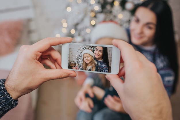 Smiling young family in Christmas atmosphere making photo with smartphone.