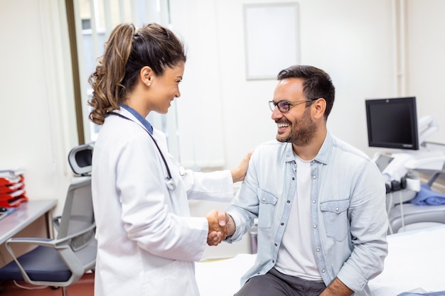 Smiling young female doctor shake hand close health insurance deal with elderly patient at consultation in hospital Happy woman GP handshake greeting get acquainted with man in clinic