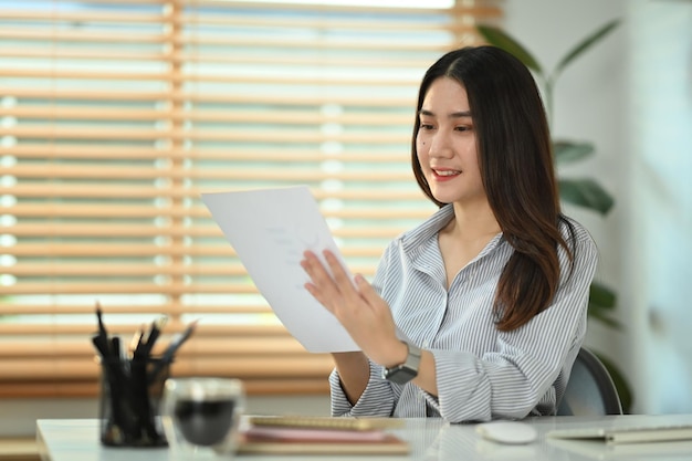 Smiling young female economist preparing report analyzing work results at workplace