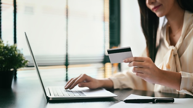 Smiling young female holding credit card and using laptop Online shopping ecommerce concept