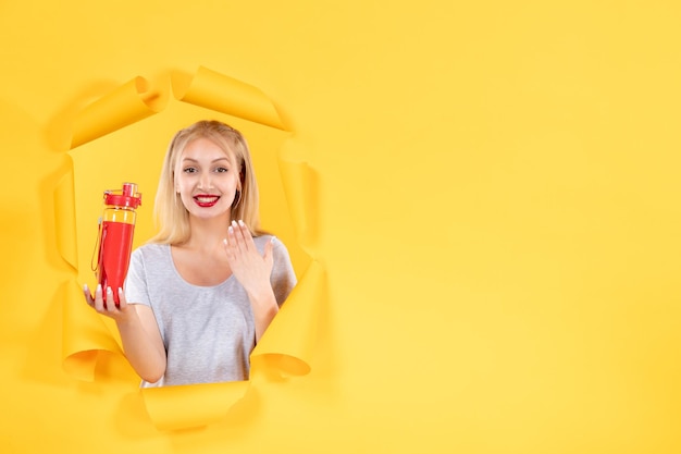 Smiling young female with red bottle on yellow wall