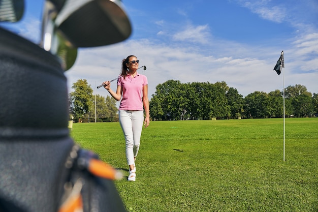 smiling young fit female in sunglasses walking across the driving range