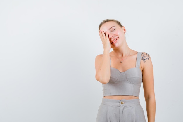 Smiling young girl covers her left eye with hands and closes her eyes on white background