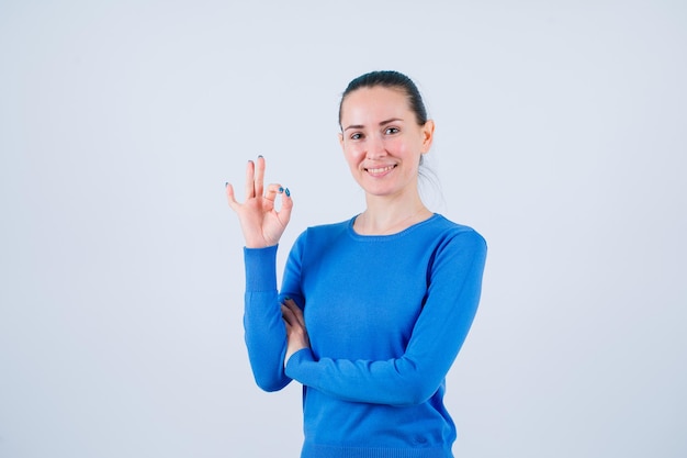 Smiling young girl is hsowing okay gesture on white background