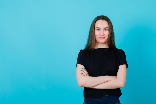 Smiling young girl is looking at camera by crossing arms on blue background