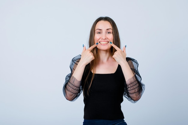 Smiling young girl is showing her smile with forefingers on white background