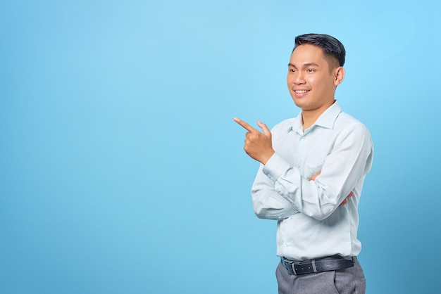 Smiling young handsome businessman pointing finger away at copy space on blue background