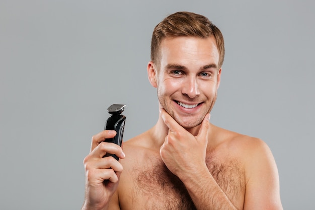 Smiling young handsome man holding razor over gray wall