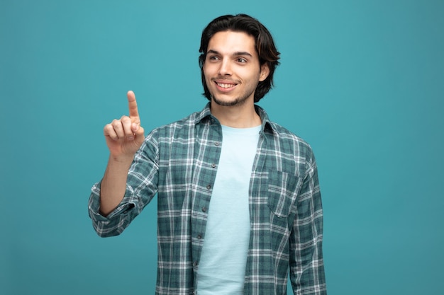 smiling young handsome man looking at side pointing up isolated on blue background