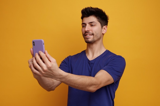 Smiling young handsome man taking selfie on yellow background