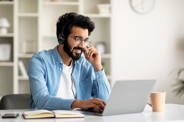 Smiling young indian man wearing headset study with laptop at home