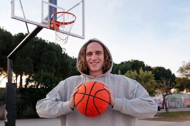 Smiling young man on a basketball court holding a ball in his hands concept of urban sport in the street copy space for text