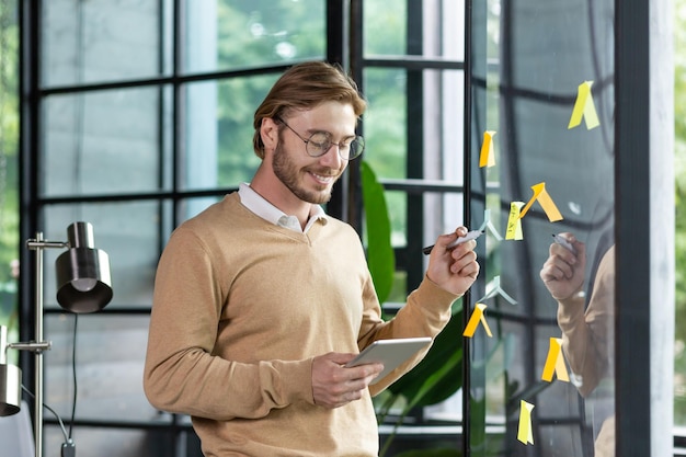 Smiling young man businessman programmer freelancer standing in the office looking at a tablet