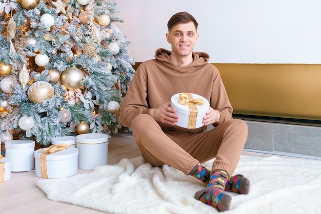 Smiling young man at Christmas near Christmas tree sitting on floor in cozy