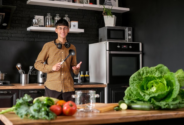 Smiling young  man cooking salad, cutting fresh vegetables in modern black kitchen