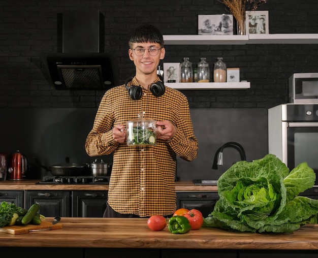 Smiling young  man cooking salad, cutting fresh vegetables in modern black kitchen