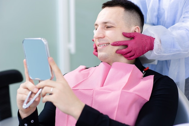 Smiling young man looking at mirror in the dentist chair.