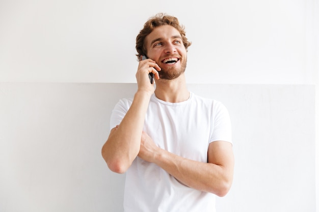 Smiling young man talking on mobile phone, standing at the wall at home