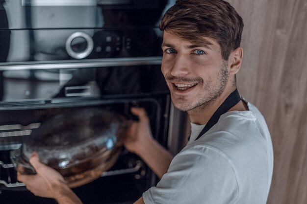 Photo smiling young man warming up dinner in his kitchen