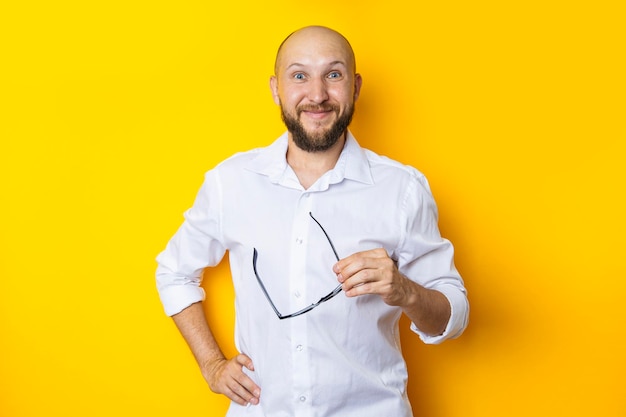 Smiling young man in white shirt holding glasses on yellow background