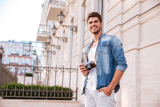 Smiling young man with old vintage photo camera standing in the city