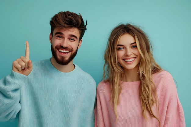 smiling young man and woman in casual sweaters man pointing up standing against blue background