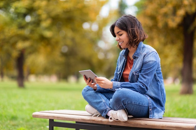 Smiling Young Middle Eastern Female Resting With Digital Tablet In Park