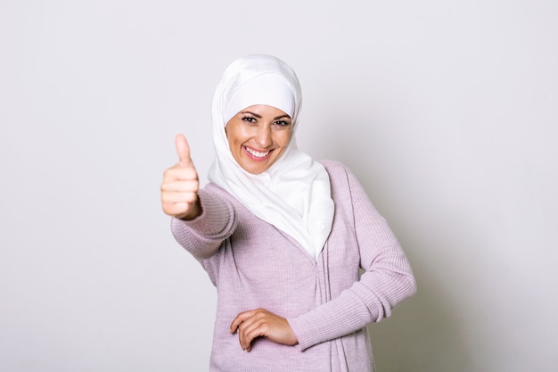 Smiling young middle eastern muslim woman looking at the camera with her thumbs up.