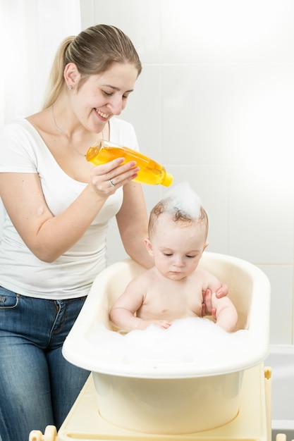 Smiling young mother washing her baby's head with shampoo