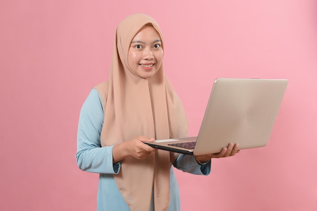 Smiling Young muslim woman using laptop isolated on pink background